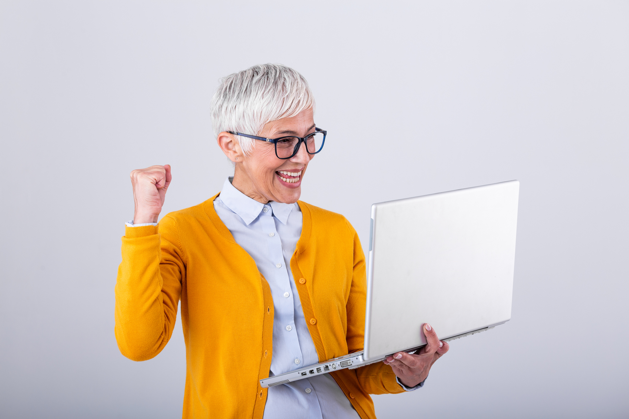 An older woman smiling while viewing her growing savings balance on a laptop.