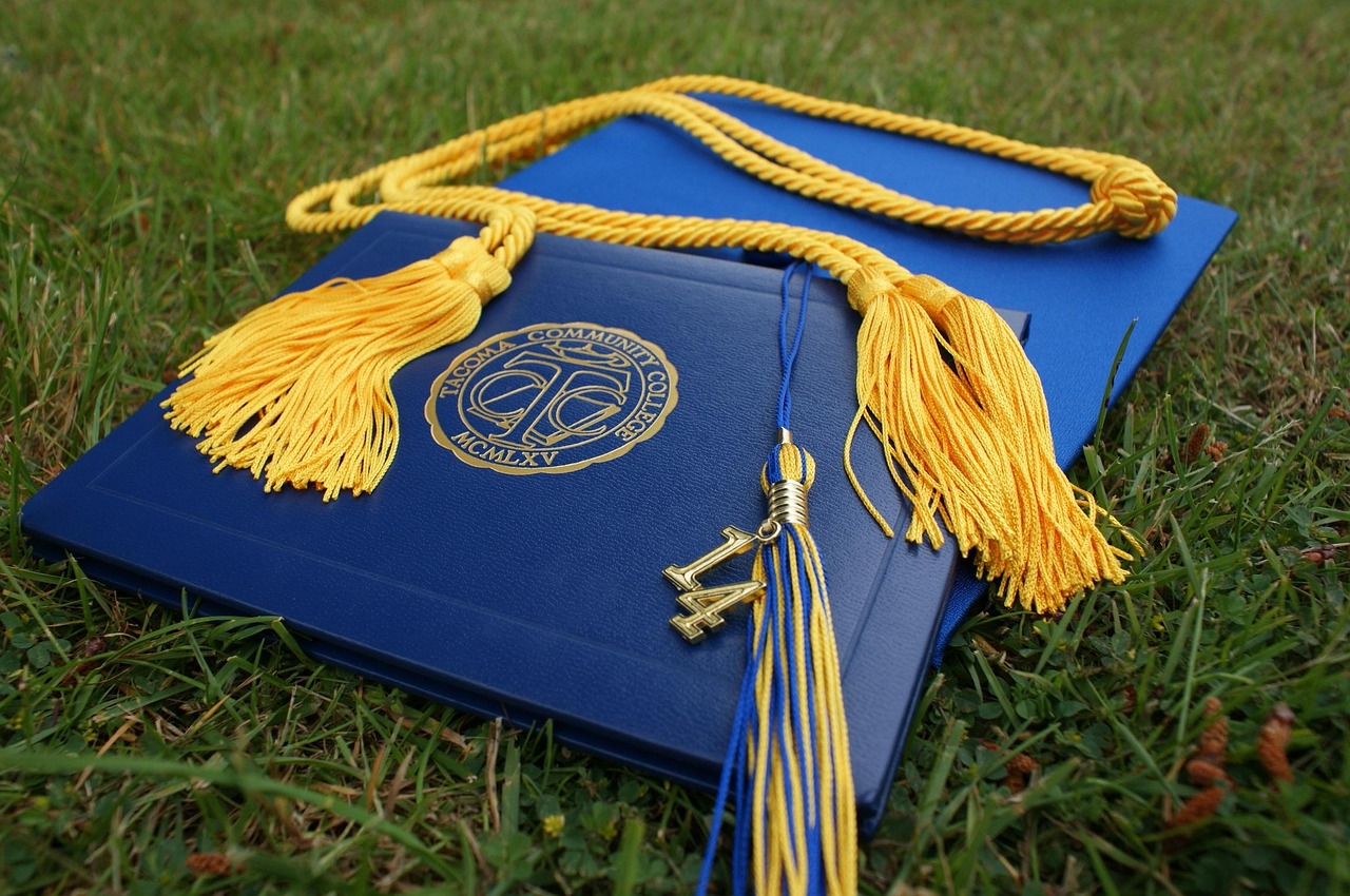 A graduation cap resting on a stack of books with a degree.