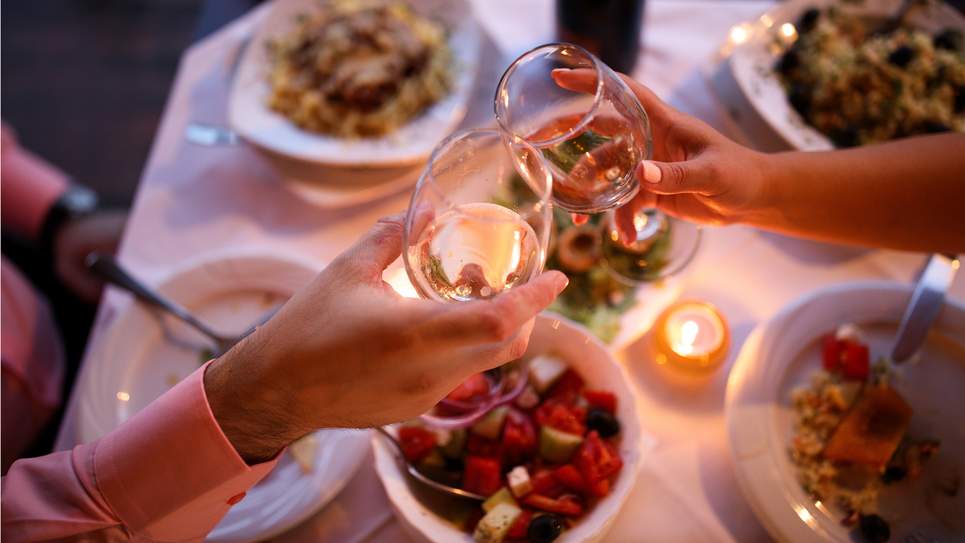 A close-up of two people toasting with wine glasses at a dim restaurant.