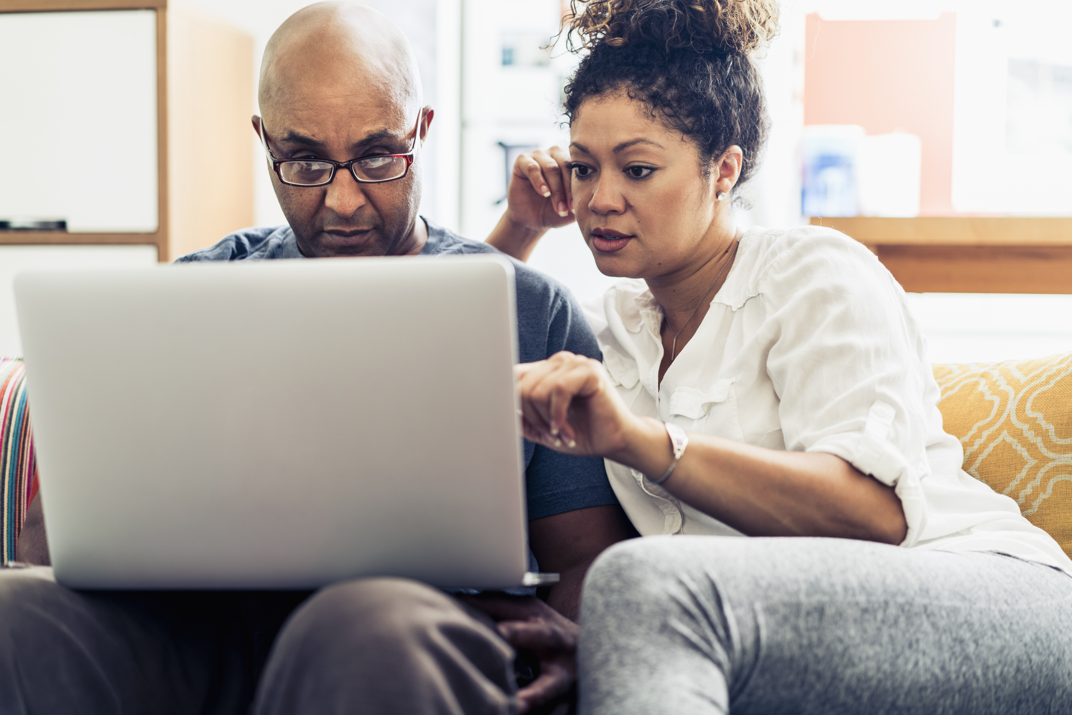A couple sitting on a sofa looking at a laptop together in a relaxed home setting.