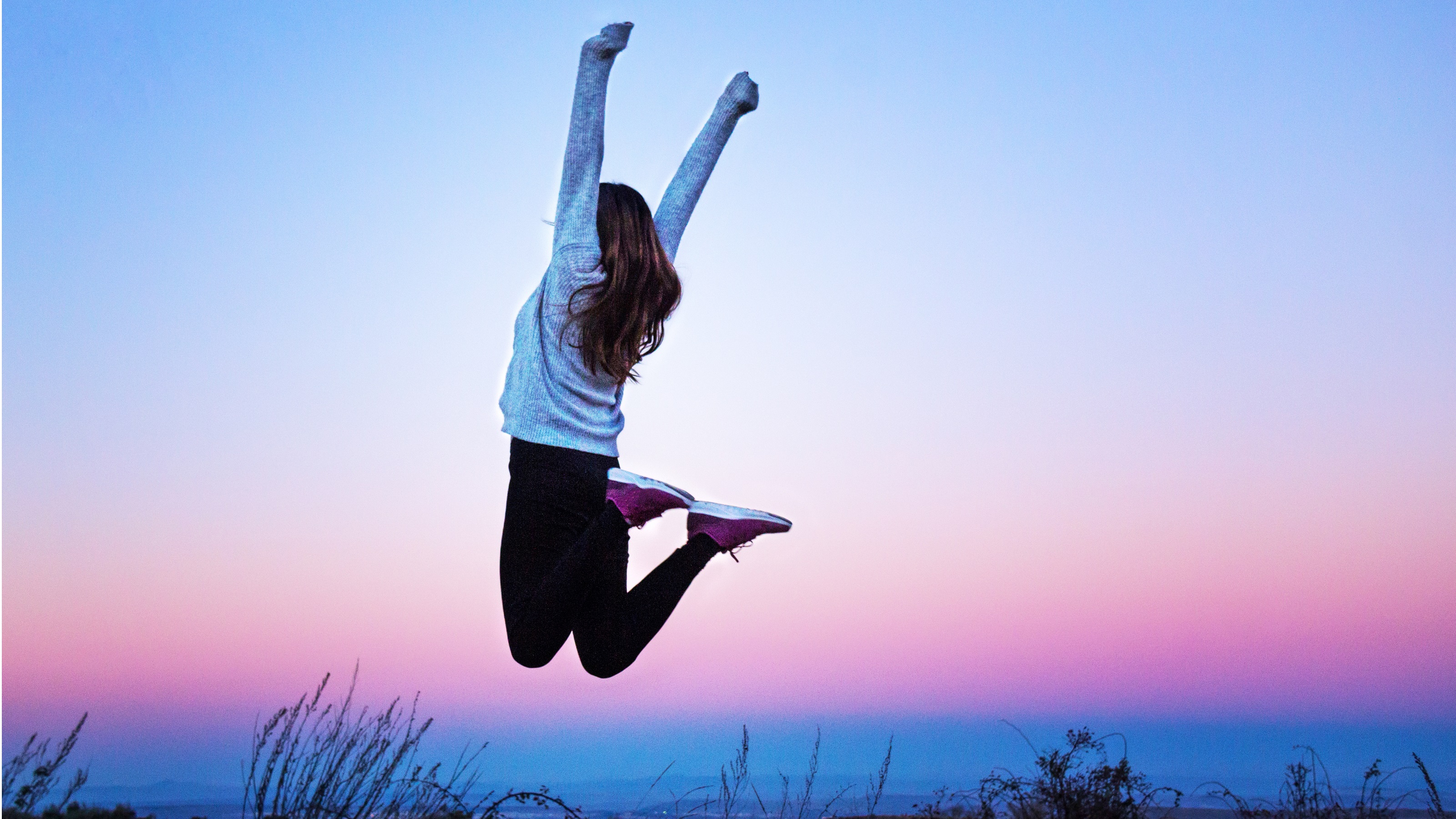 A woman jumps in the air with arms raised in a gesture of financial freedom and success.