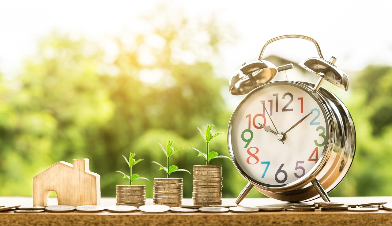 An hourglass next to stacked coins and a small plant representing long-term dollar cost averaging and compound interest.