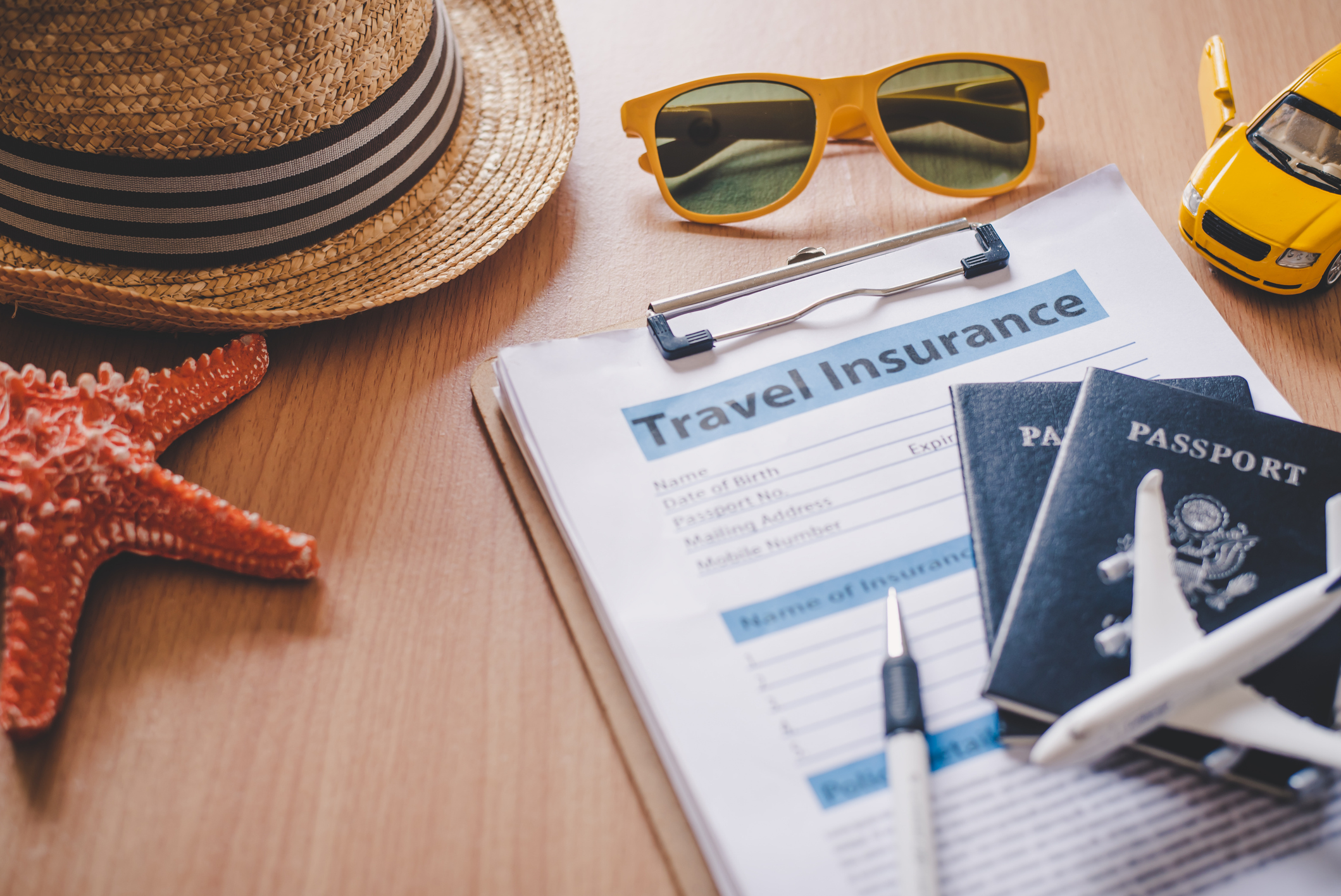A travel hat, starfish, and passport resting on top of a travel insurance application form.