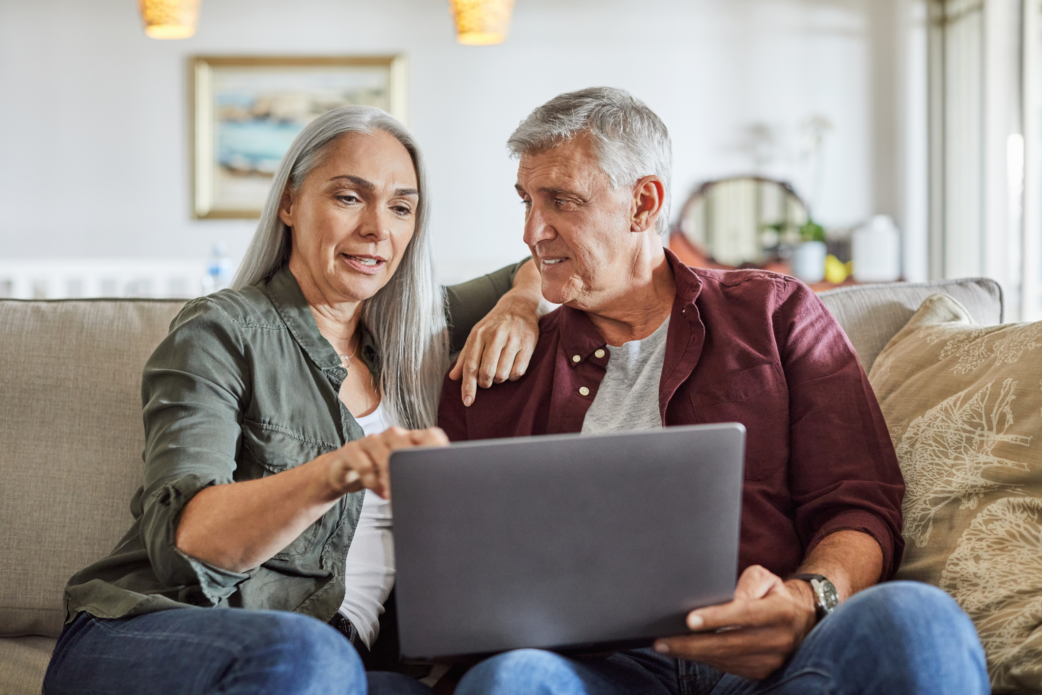 A mature couple sitting comfortably on a sofa in a modern living room while looking at a laptop together