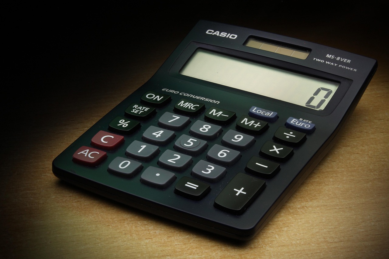 An overhead view of a calculator, a cup of coffee, and stacks of currency notes.
