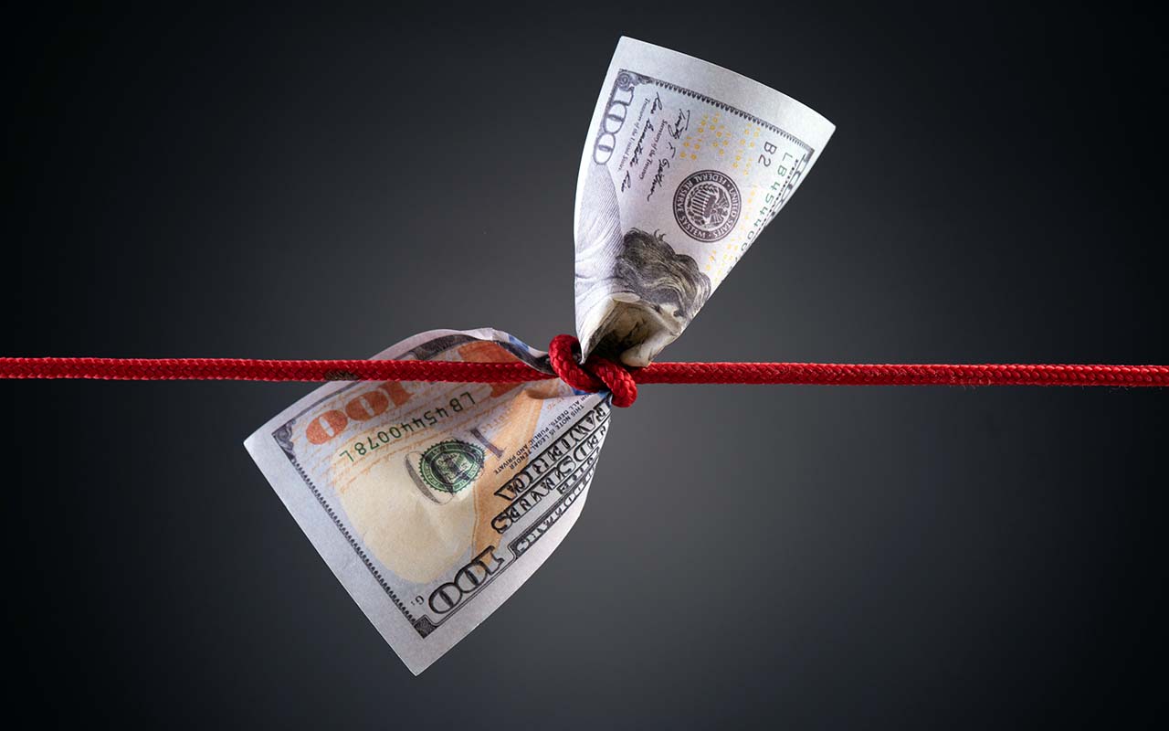 A dollar bill tied in a tight red rope knot representing financial complexity.