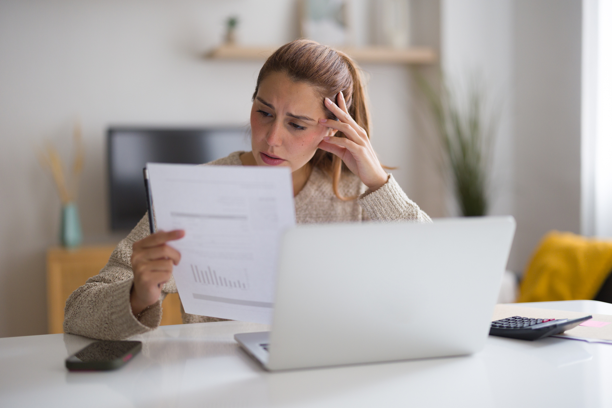 A woman looking distressed and surprised while examining a high monthly energy bill.