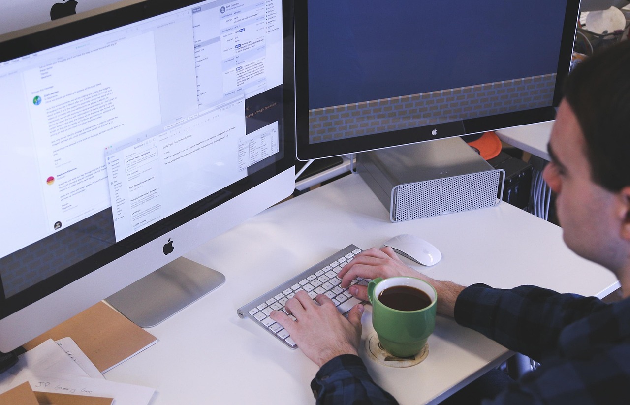 A person checking a watch while working at a computer desk.