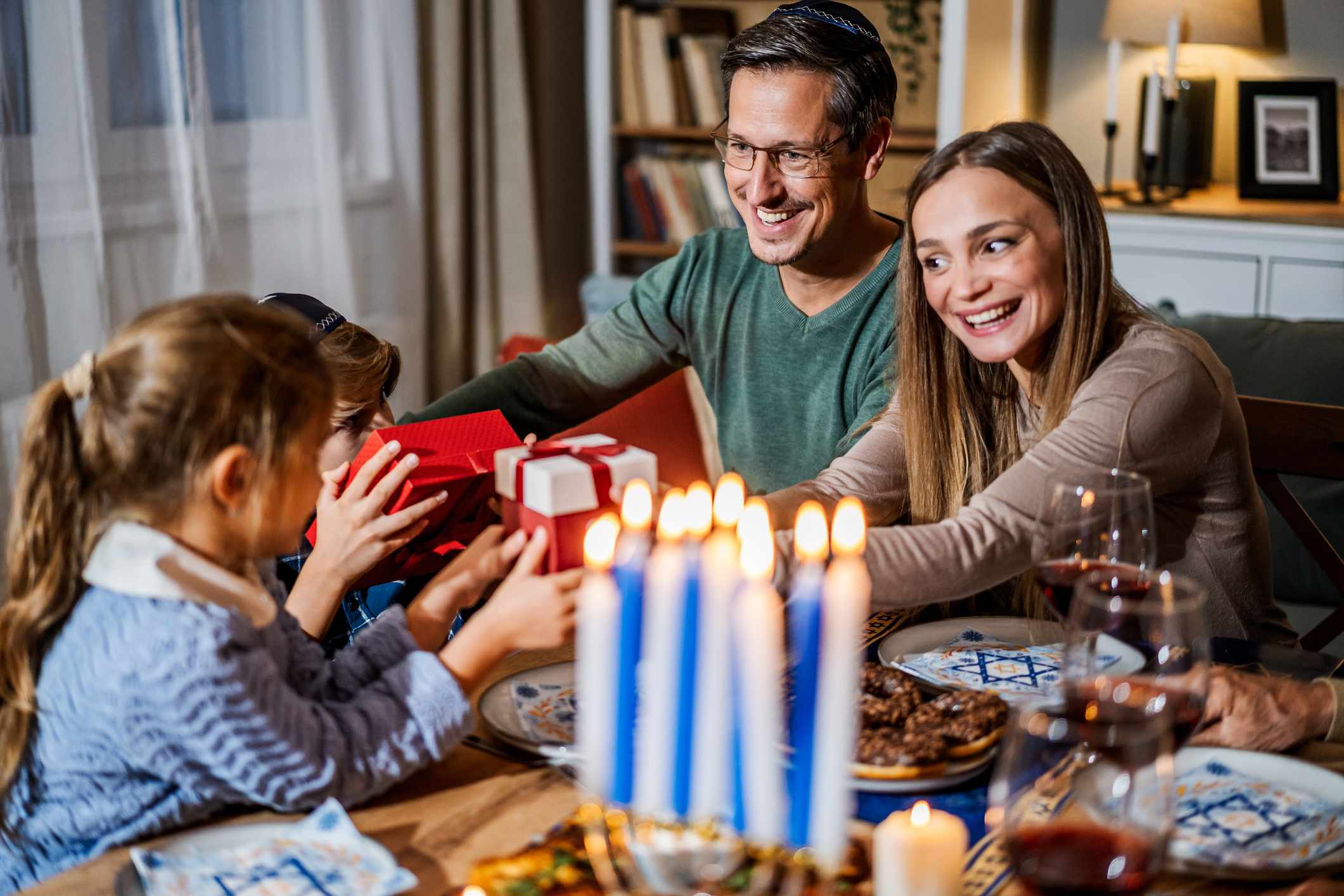 A multi-generational family celebrating together as a child passes a gift during Hanukkah.