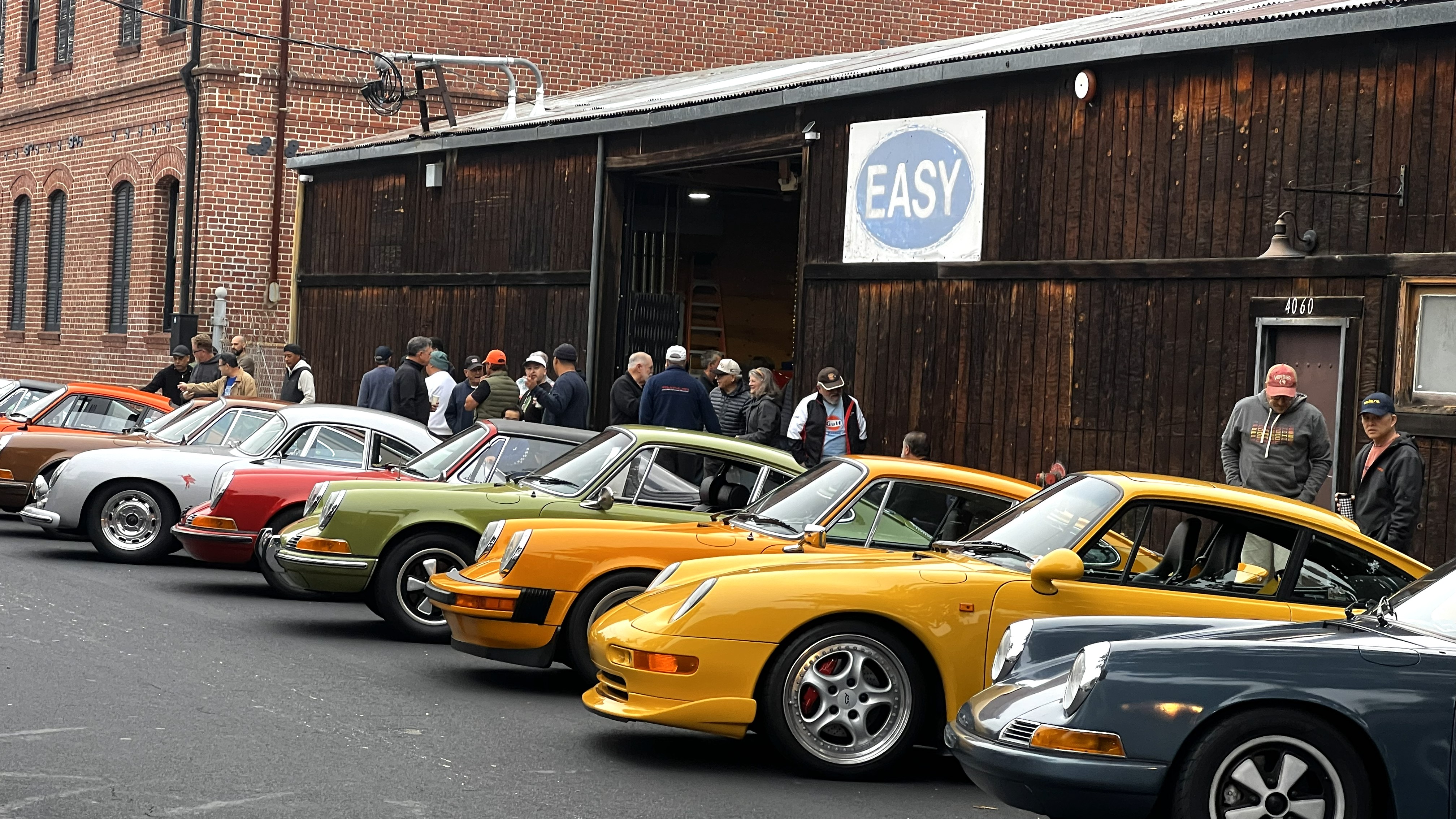 A row of colorful classic Porsche and other vintage cars parked at an outdoor enthusiast gathering.