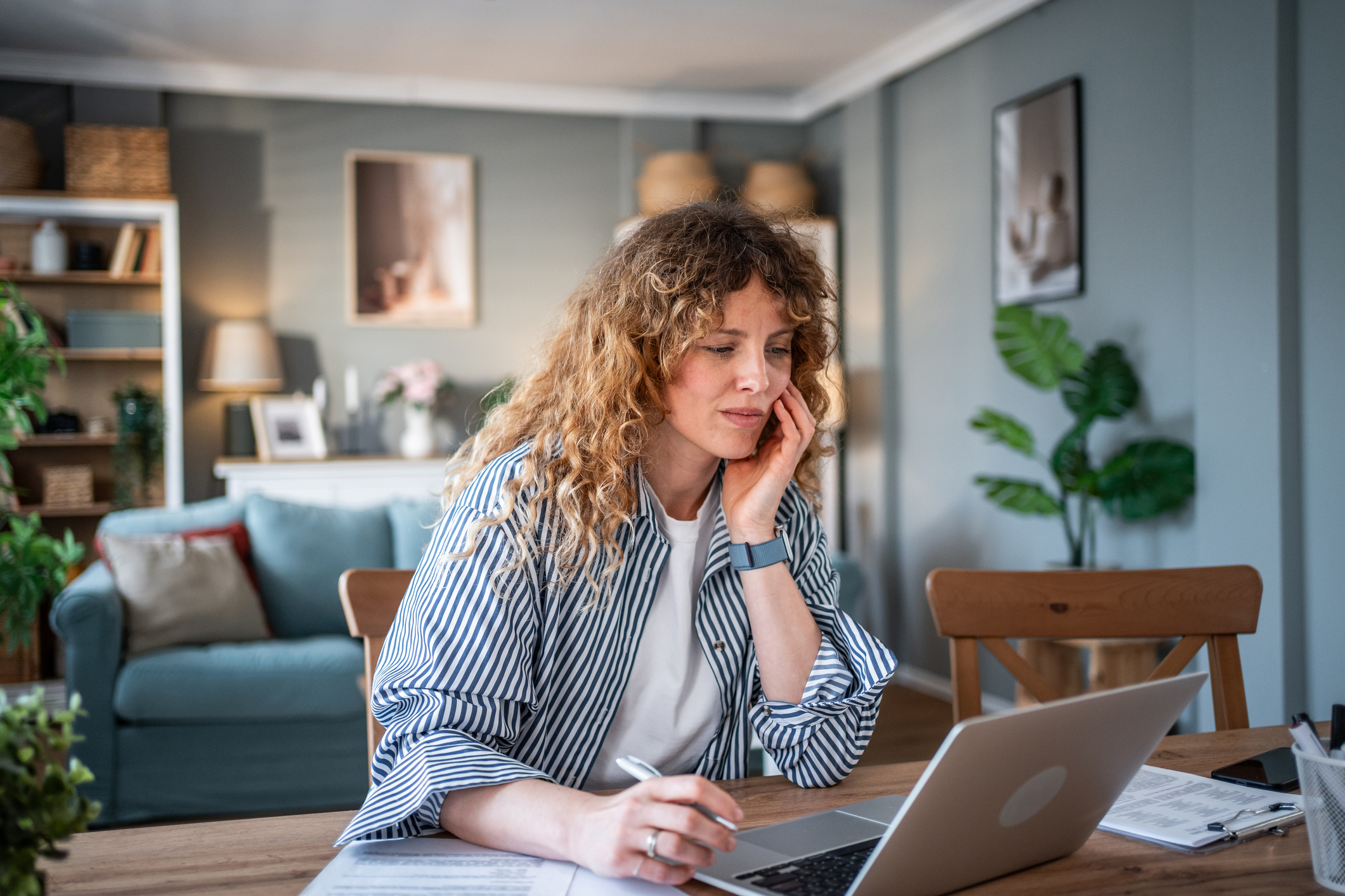A woman doing research on her laptop sitting at a table in a bright room.