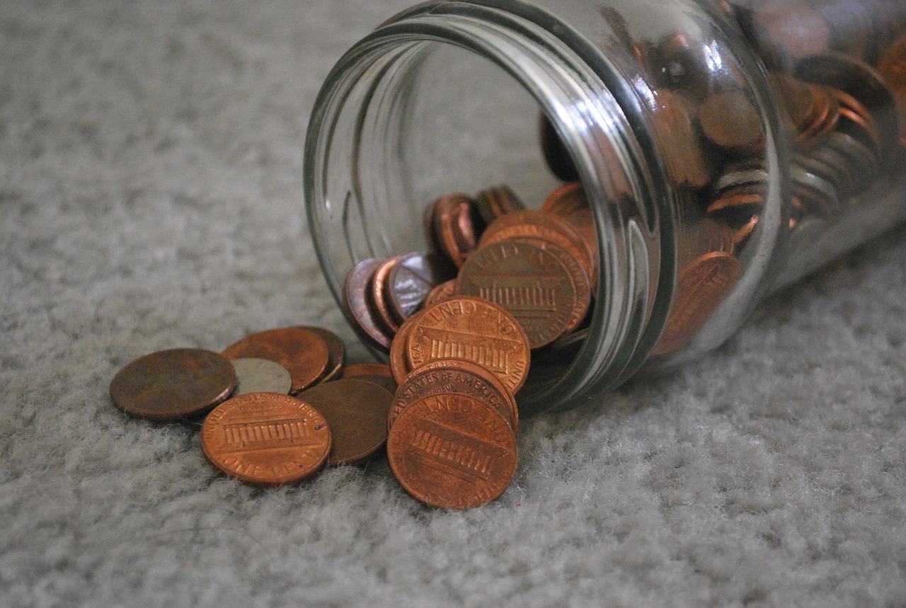 A small umbrella sheltering a glass jar full of coins to represent a financial safety net.