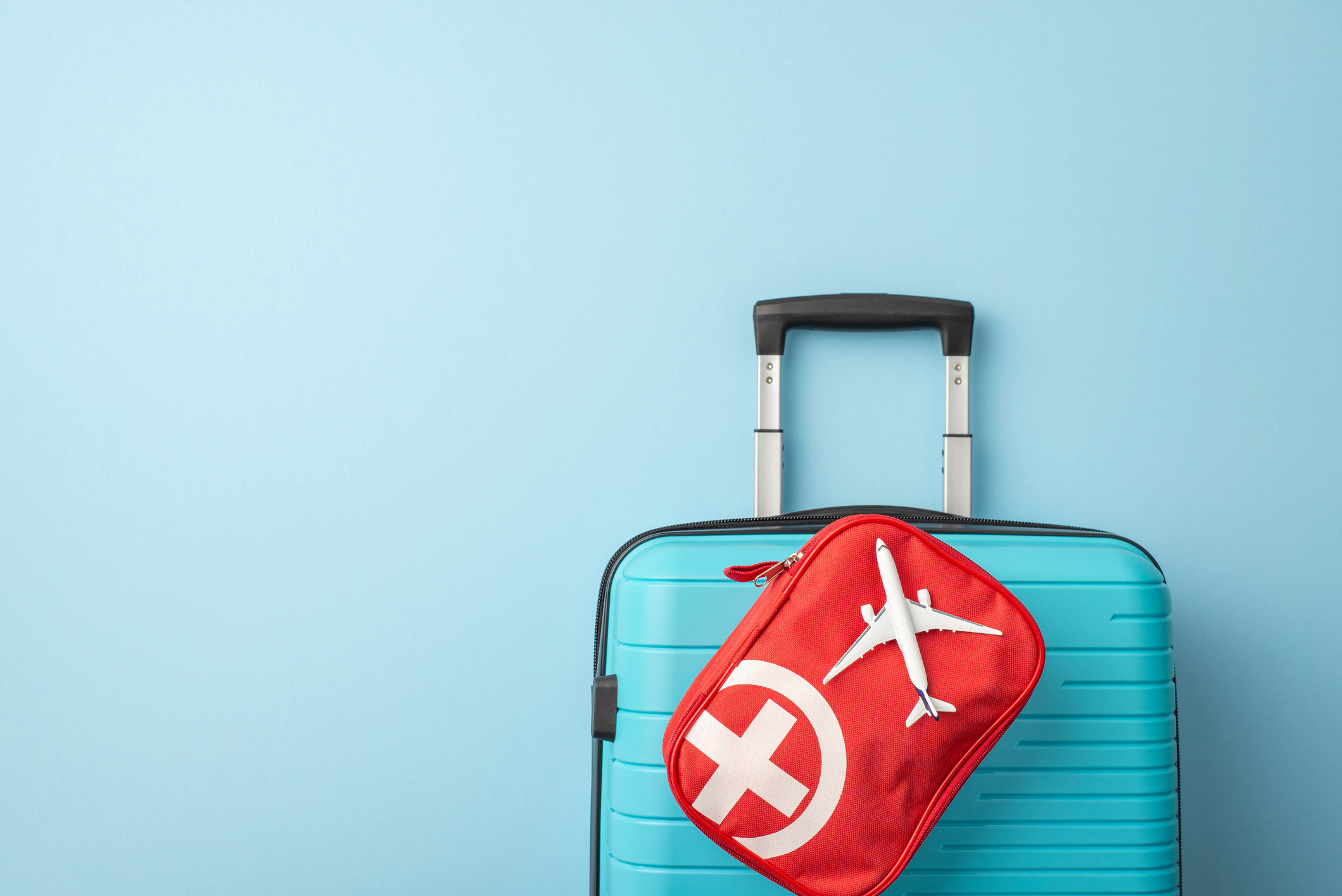 A silver suitcase with a red and white first aid kit attached and visible.