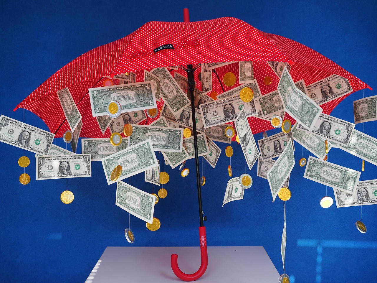 A yellow umbrella protecting a pile of coins from falling rain, symbolizing a financial cushion.