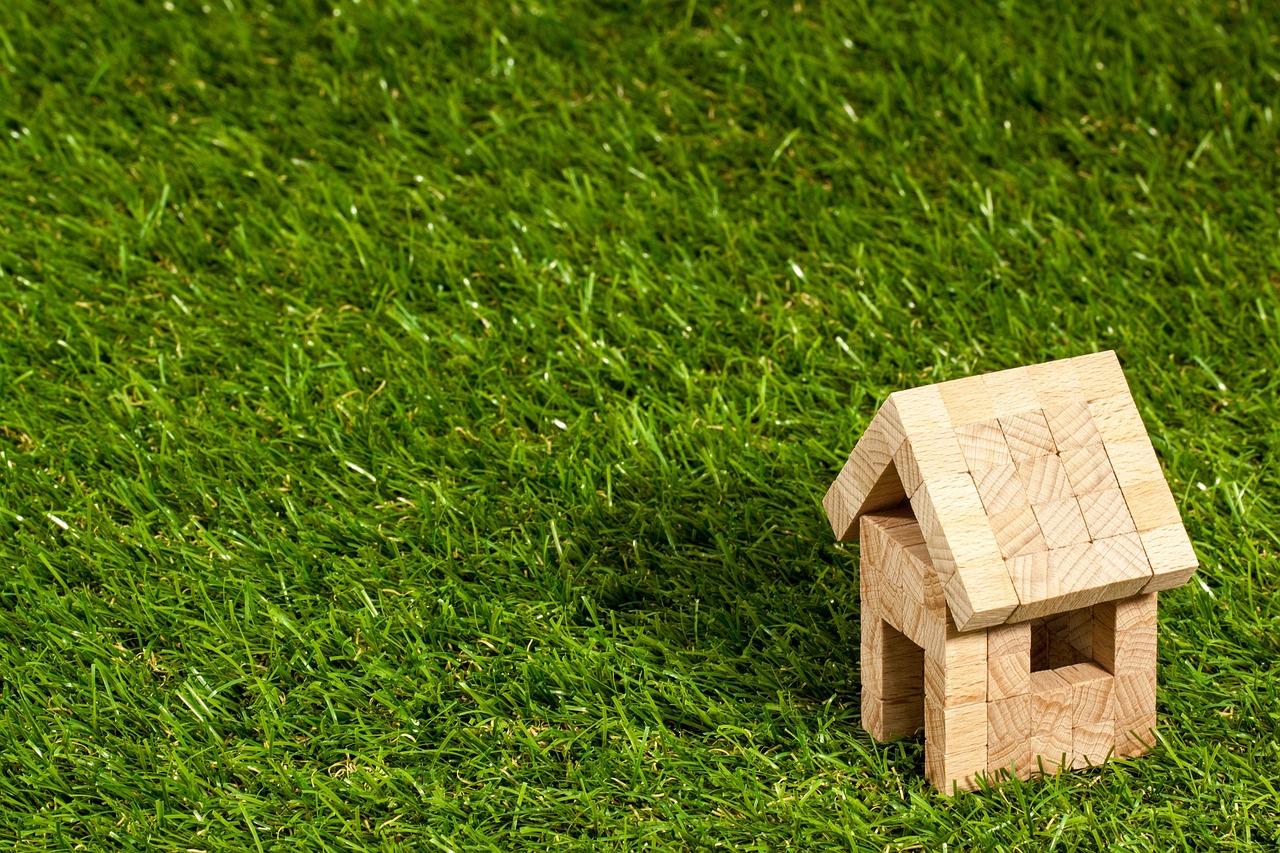 A small wooden model of a house sitting on a desk alongside financial charts.