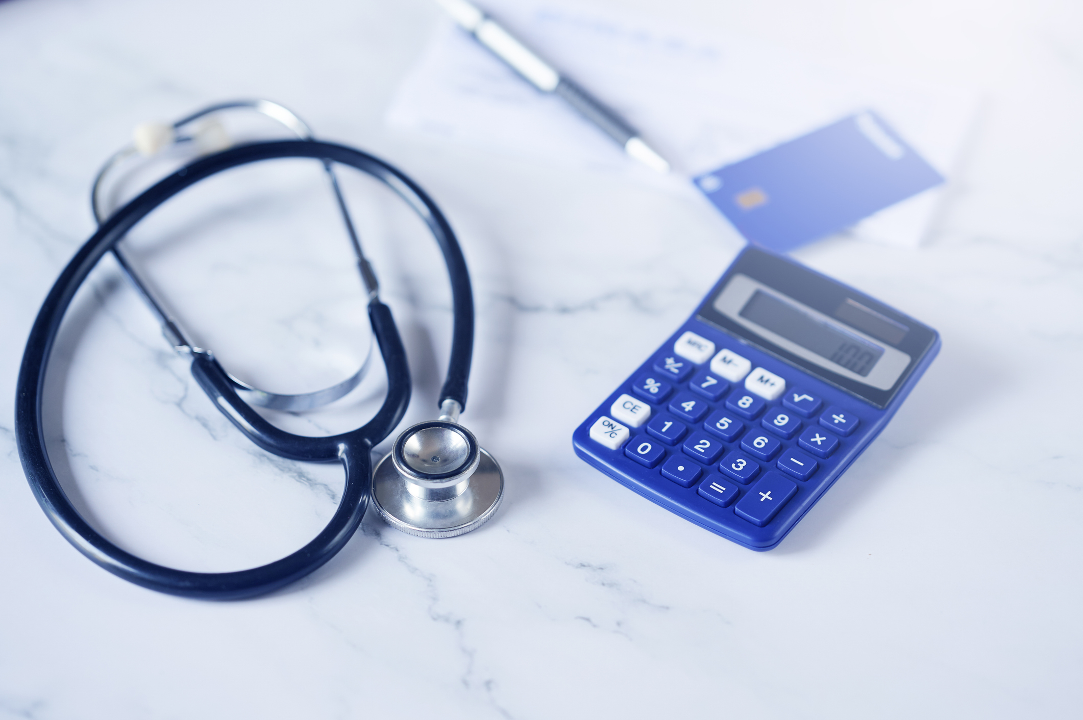A stethoscope resting next to a credit card and a calculator on a desk.