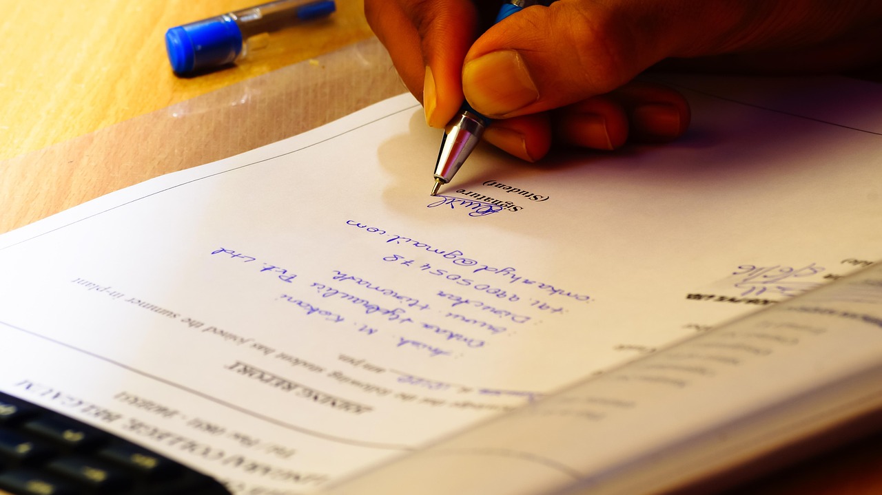 A close-up of a person signing a bank check on a professional wooden desk.