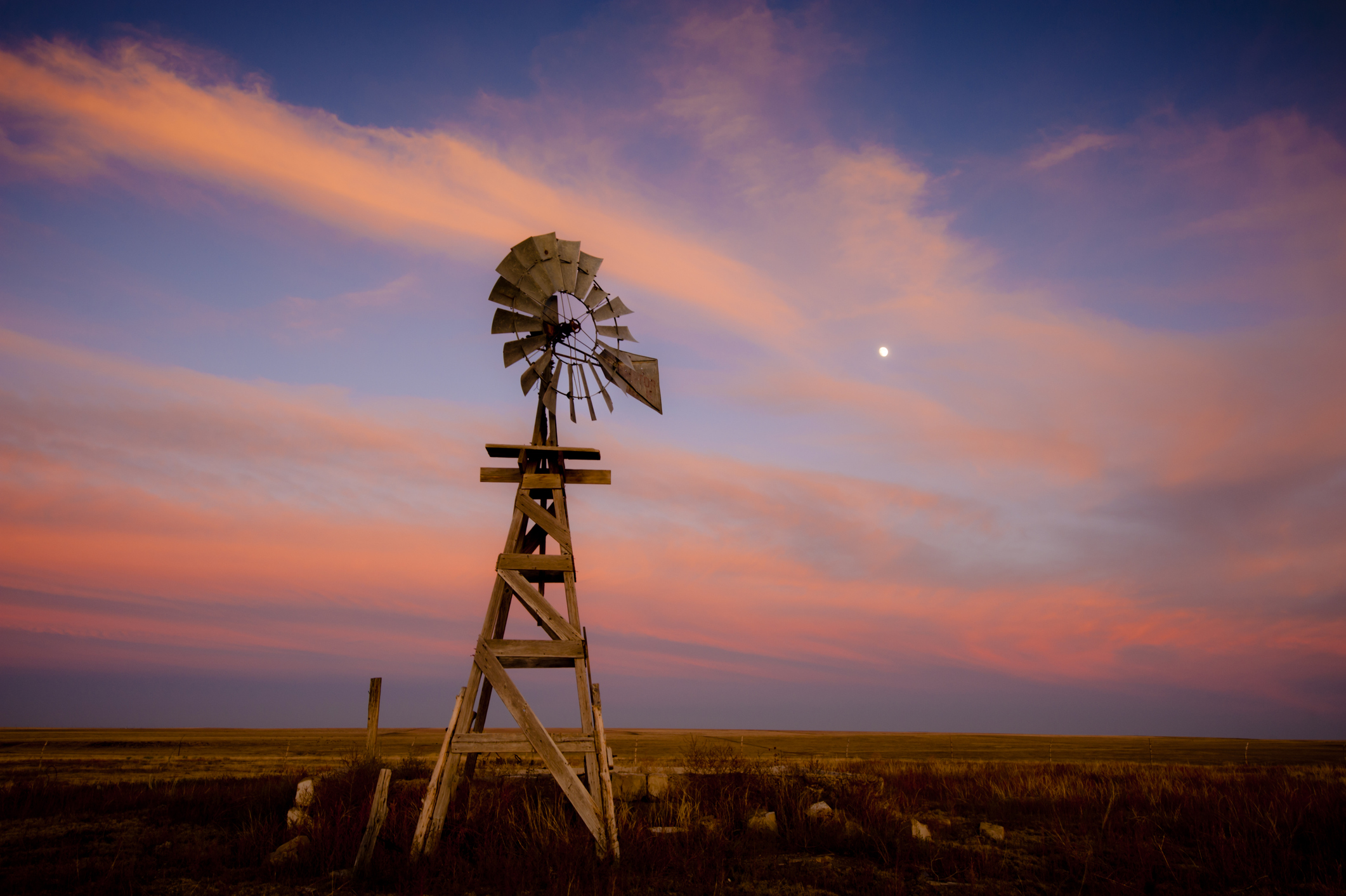 A vintage wooden windmill silhouetted against a pink and purple sunset sky in Lamar, Colorado.