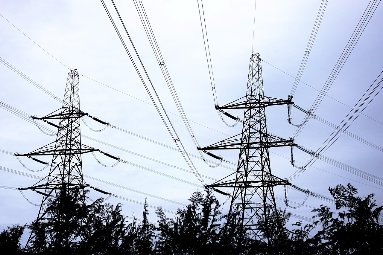 Transmission towers and power lines against a sunset sky symbolizing energy demand.