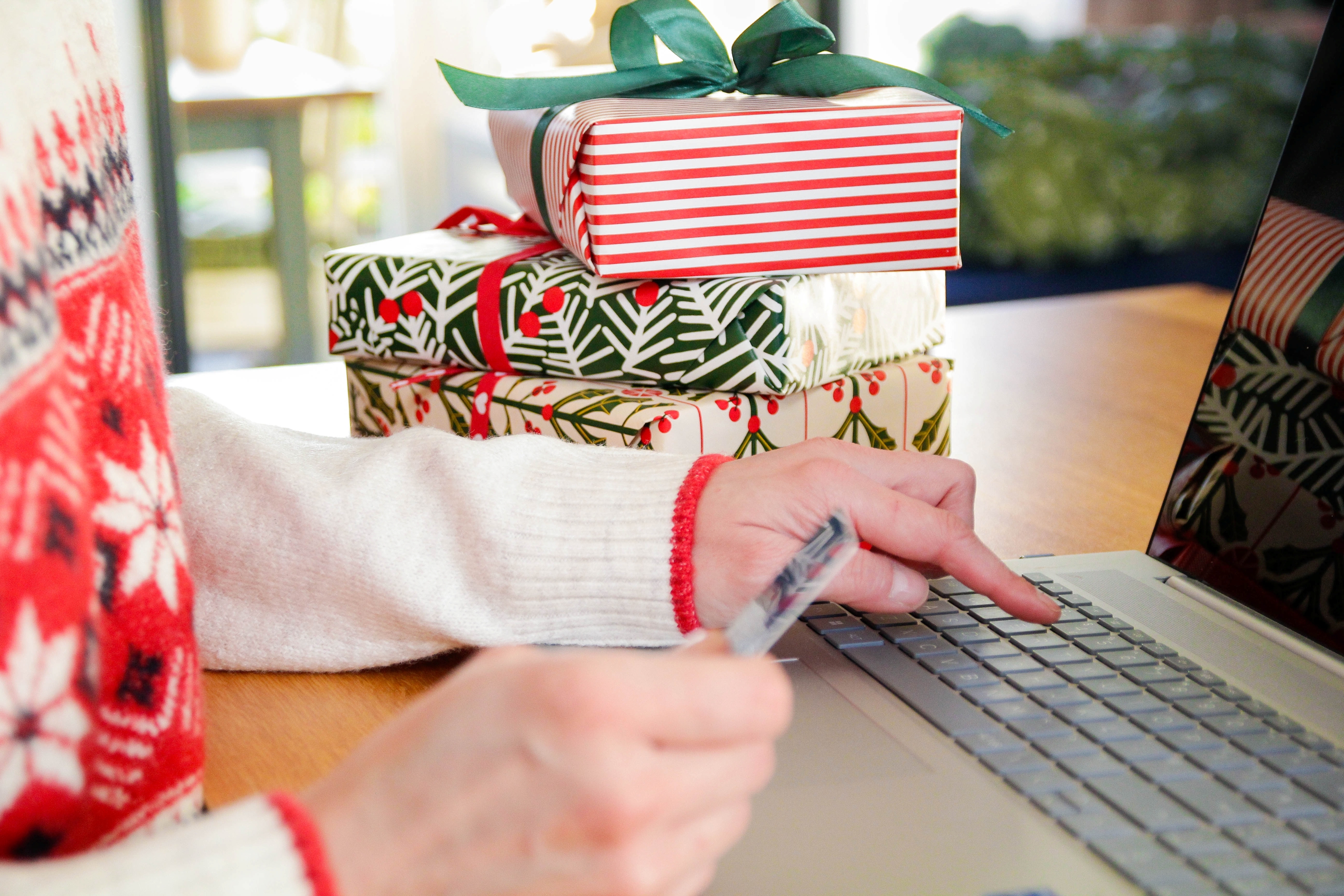 A woman typing credit card information into a laptop next to stacked gift packages.