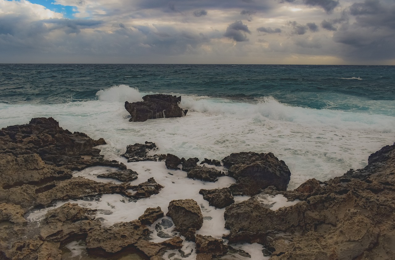 Powerful ocean waves crashing against dark jagged rocks during a storm.